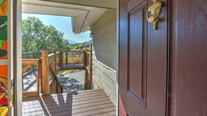A wooden staircase leading to a covered porch with a view of trees and mountains in the background.