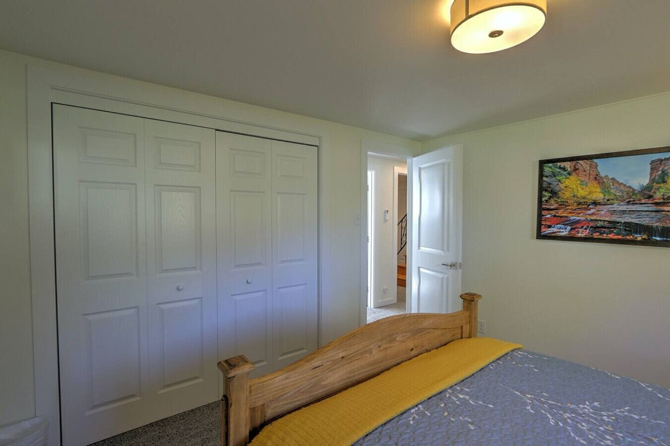 Une chambre à coucher avec un lit en bois, une porte double blanche et un tableau représentant un paysage.