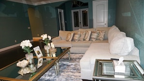 Una sala de estar con un sofá color beige, una mesa de centro de vidrio y una alfombra estampada.