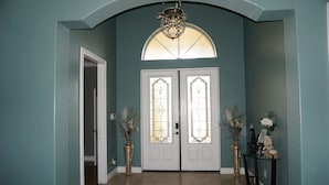 Un pasillo con paredes color turquesa, un candelabro y dos puertas dobles con vidrieras.