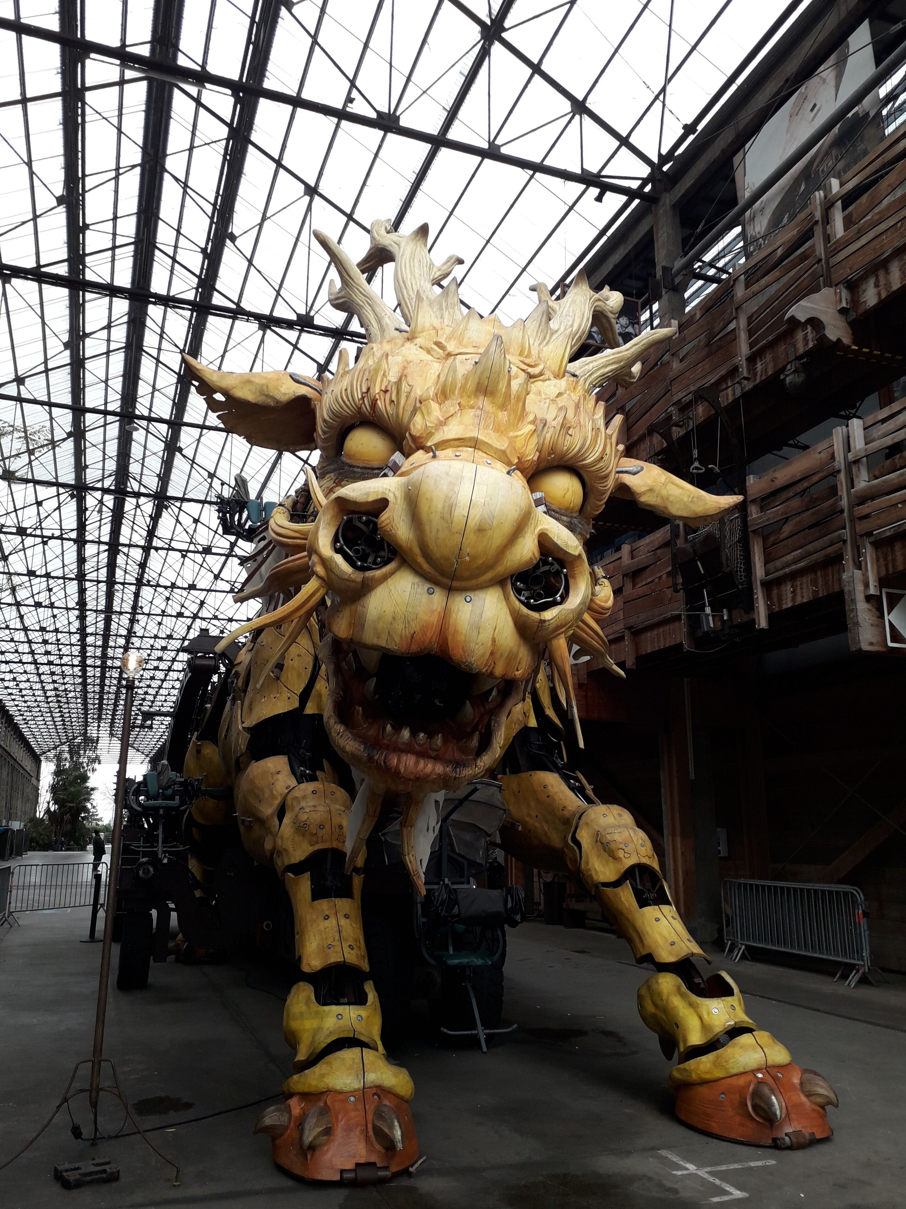 A large, intricately carved wooden dragon statue in a covered indoor space with a high ceiling and metal railings.