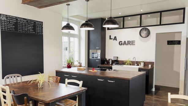 A modern kitchen with a central island, pendant lights, and a dining area with chairs.