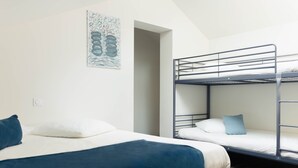 A dormitory room with bunk beds, a bed with a blue blanket, and a wall-mounted artwork.