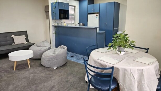 Un espacio habitable compacto con kitchenette, zona de comedor y asientos que incluyen un sofá y pufs.