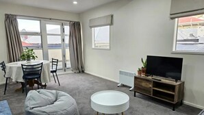 Una sala de estar con comedor, un televisor sobre un mueble de madera y vistas al exterior.