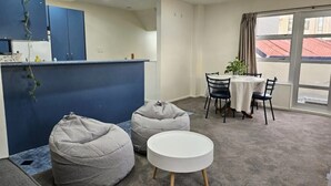 Una habitación moderna con comedor, dos sillones tipo bean bag grises, una pequeña mesa blanca y una ventana con vistas a edificios.