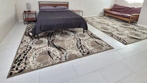 Ein Schlafzimmer mit einem Bett, einem Nachttisch, einem Deckenventilator, einem Sofa und einem gemusterten Teppich.
