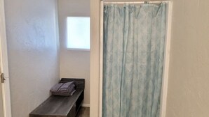 Ein kleines Badezimmer mit Duschvorhang, einer Bank und einem Fenster.