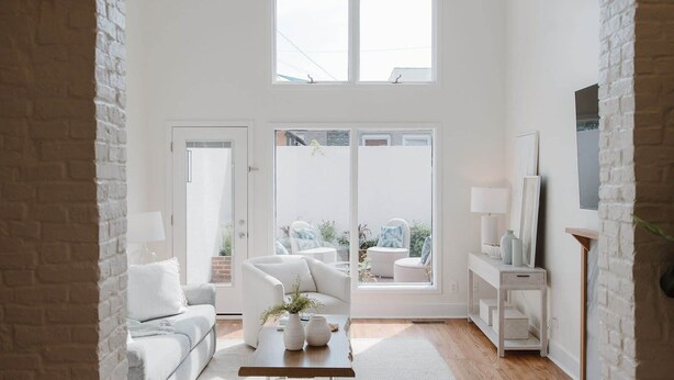 Un intérieur lumineux et blanc, avec un canapé, une table basse et une vue sur l’extérieur grâce à de grandes fenêtres.