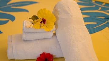 Una toalla blanca doblada con cuidado y una flor de hibisco rojo sobre una colcha amarilla con motivos florales azules.