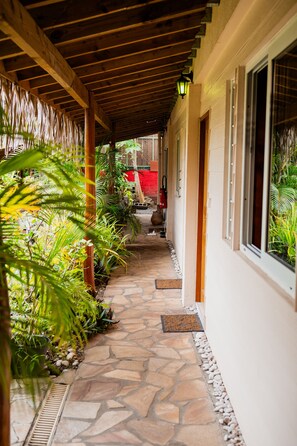 Walkway leads to a building entrance surrounded by lush greenery and a wooden structure.