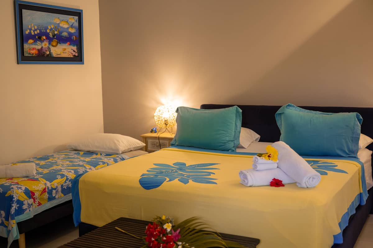 Habitación de hotel con dos camas, una mesita de noche con lámpara, una pequeña mesa con flores y un cuadro en la pared.