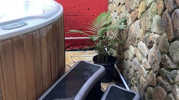 Un jacuzzi con escalones, una pared roja y una pared de piedra con plantas.