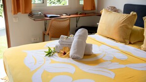 Uma cama bem arrumada com toalhas e uma flor, uma escrivaninha com uma cadeira e uma janela com cortinas.
