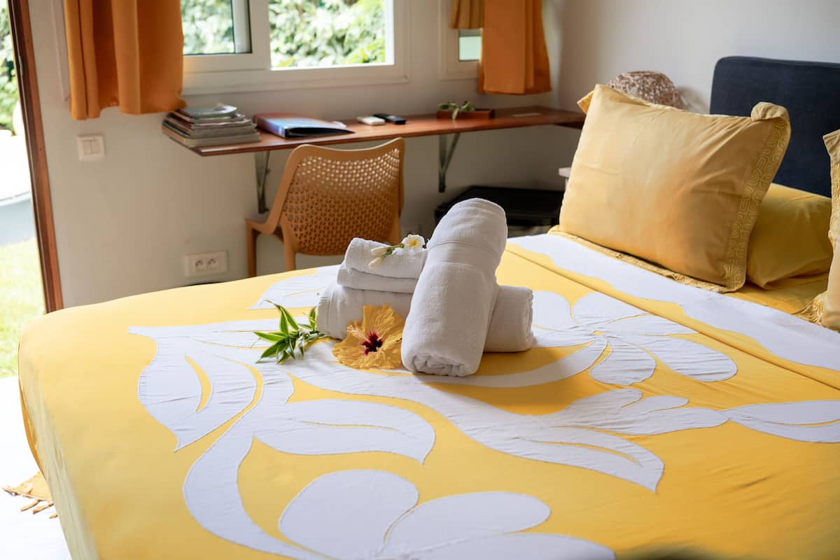 Una cama bien hecha con toallas y una flor, un escritorio con una silla, y una ventana con cortinas.