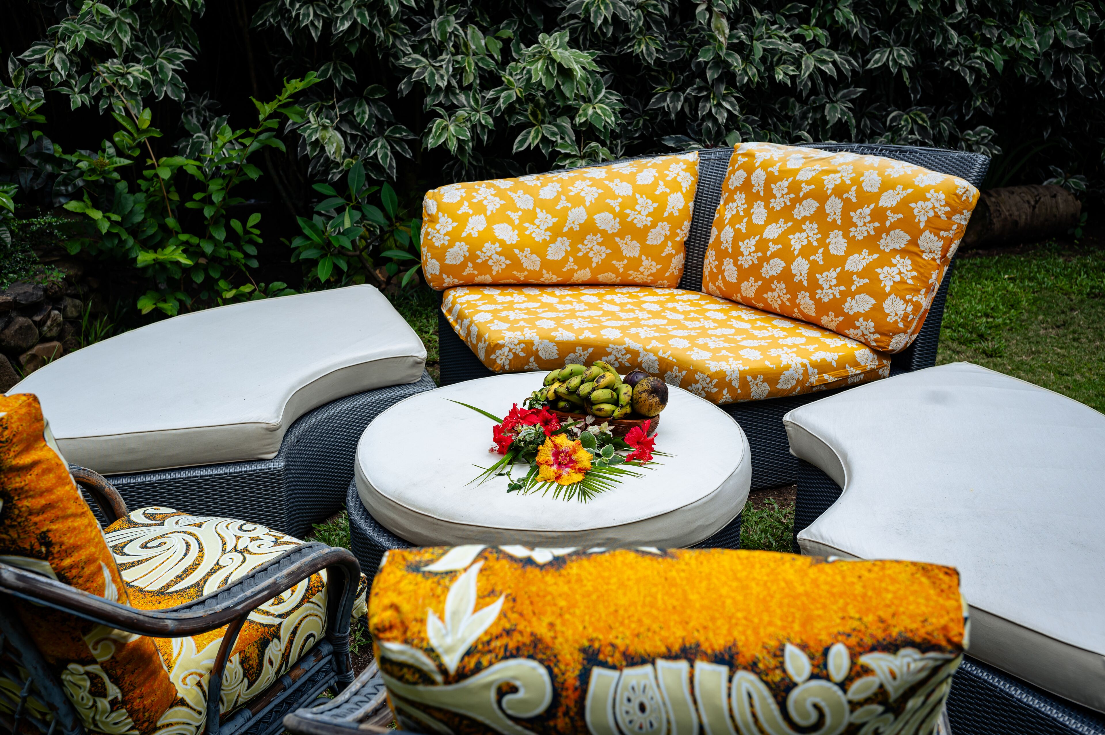 Un espace aménagé dans le jardin, avec des meubles en osier et une table ronde centrale agrémentée d’un arrangement floral.