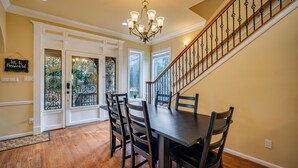 Un espace repas comprenant une table et des chaises en bois, un lustre et un escalier muni d’une rampe.