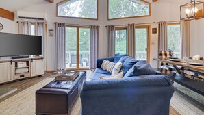 A spacious living room with a large blue sofa, a flat-screen TV, and a dining area with a wooden table and chairs.