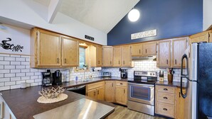 A modern kitchen with wooden cabinets, stainless steel appliances, and a coffee-themed wall.