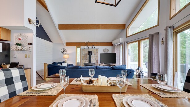 A dining area with a wooden table set for four, a blue sofa in the background, and a stone fireplace.