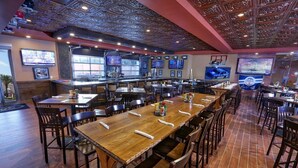 Ein Restaurant mit mehreren Holztischen und -stühlen, einer Bar und Bildschirmen, die Sportübertragungen zeigen.