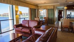 Ein Hotelzimmer mit einer Ledersofa, einem Esstisch mit Stühlen, einer Küchenzeile und großen Fenstern mit Blick auf ein Gewässer.
