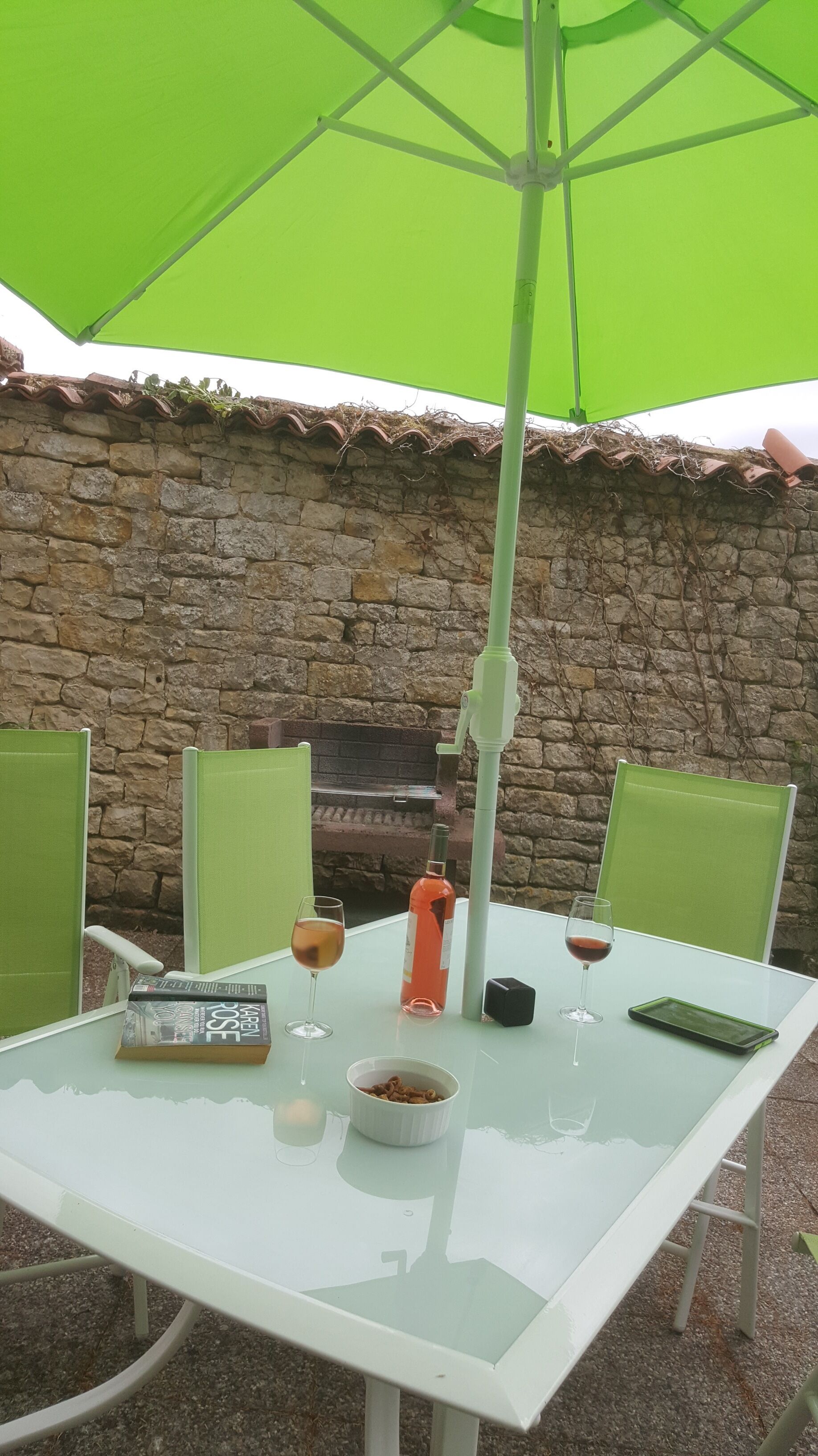 Ein Tisch mit Glasplatte, umgeben von grünen Stühlen, unter einem grünen Sonnenschirm.