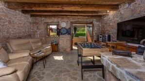 A cozy room with a stone wall, a leather sofa, a foosball table, and a television. - Amazing home in Polje (Polje)