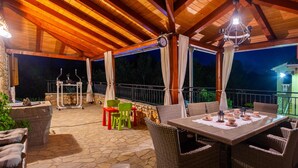 An outdoor covered patio with stone flooring, wicker furniture, and a table set for dining. - Amazing home in Polje (Polje)
