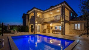 Une maison à deux étages dotée d’une piscine, d’une façade en pierre et d’un espace extérieur aménagé pour se détendre.