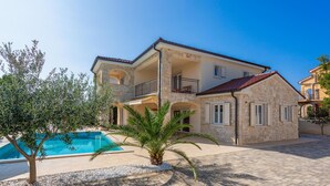 Une maison en pierre à deux étages, dotée d’une piscine, d’un balcon et d’un jardin agrémenté d’un palmier.
