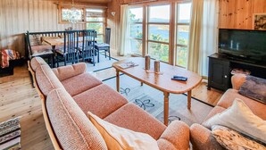 A cozy cabin interior with a long sofa, a dining table, and a TV. - Cozy home in Kjørsvikbugen with WiFi (Kjørsvikbugen)