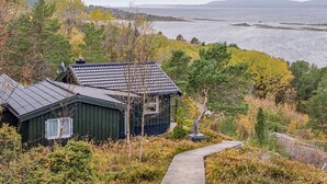 A coastal cabin with a sloped roof, surrounded by dense vegetation and a clear view of the ocean. - Cozy home in Kjørsvikbugen with WiFi (Kjørsvikbugen)