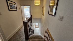 Un couloir avec un escalier recouvert de moquette menant à une pièce où se trouvent un lit et une fenêtre.