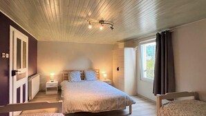 Ein Schlafzimmer mit Holzbalkendecke, einem Bett mit weißer Bettdecke, zwei Nachttischlampen, einem Fenster mit Vorhängen und einem Holzstuhl.