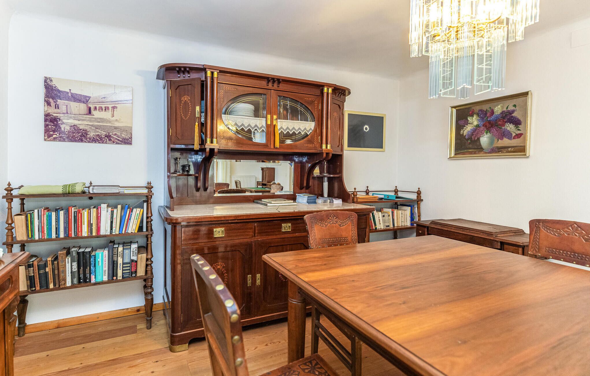 Uma sala de estudo com uma mesa de madeira, estantes, um grande armário de madeira e um candelabro.