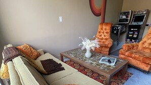 A living room with a beige sofa, orange armchairs, a coffee table with a vase, and a large abstract painting on the wall. - New Lovely Home in Lockhart with a Lounge (Lockhart)