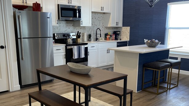 A modern kitchen with white cabinets, stainless steel appliances, a central island with stools, and a hanging light fixture. - New Lovely Home in Lockhart with a Lounge (Lockhart)