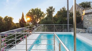 A swimming pool with a metal railing, surrounded by greenery and a stone wall.