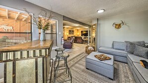 A modern living room with a grey sofa, a wooden coffee table, and a bar area with stools.