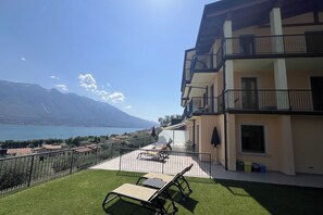 Un balcón con vistas a un lago y montañas, muebles de exterior y un edificio con balcones.