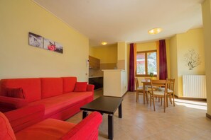 A living room with a red sofa, a dining table with chairs, and a kitchen area in the background. - "Villa Imelda" spacious, bright apartments, garden or balcony, lake view (Limone Sul Garda)