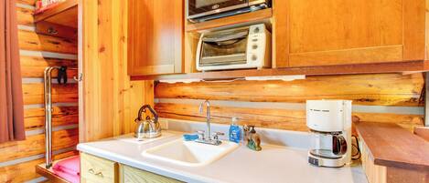 Cocina compacta con armarios de madera, microondas, horno tostador, lavabo y cafetera.