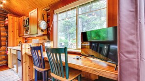 A wooden cabin interior with a kitchen area, a dining table with chairs, and a large window providing a view of the outdoors. - Montana Mountain Getaway - 1 Mi to Yellowstone! (Silver Gate)
