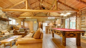 Ein Blockhaus-Interieur mit Billardtisch, Ledersofa und Kamin aus Stein.