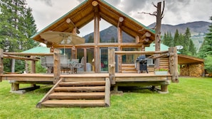 Eine Blockhütte mit einer Terrasse, Sitzgelegenheiten im Freien und einem Berg im Hintergrund.