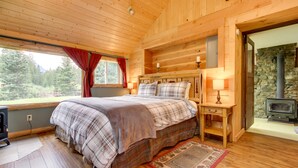 Ein Schlafzimmer in einer Holzhütte mit einem Bett, einem Nachttisch, einer Lampe und einem Kamin aus Stein.