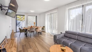 En moderne stue med en grå sofa, et træspisebord og et tv ophængt på væggen.