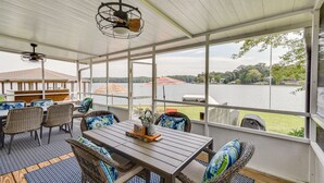 Eine überdachte Terrasse mit Tisch und Stühlen, große Fenster mit Blick auf einen See und Bäume.