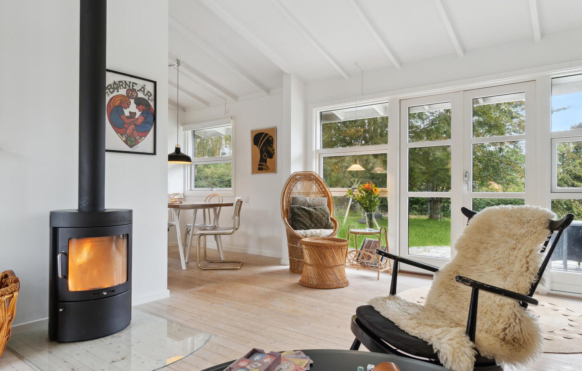 A cozy living room with a wood-burning stove, wicker furniture, and large windows offering a view of the outdoors.